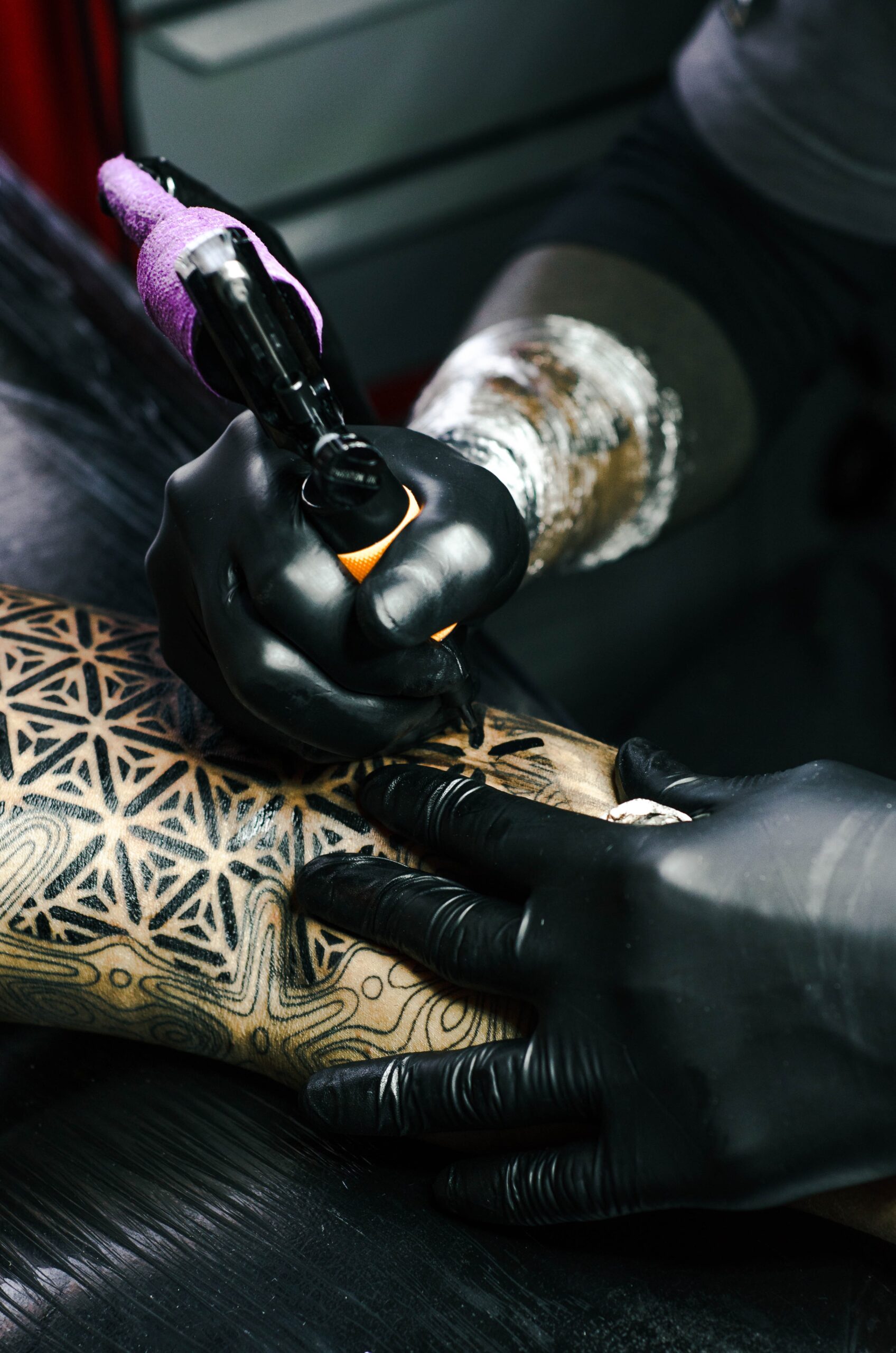 Tattoo artist with black shirt and black gloves tattooing a beautiful all black geometric tattoo.